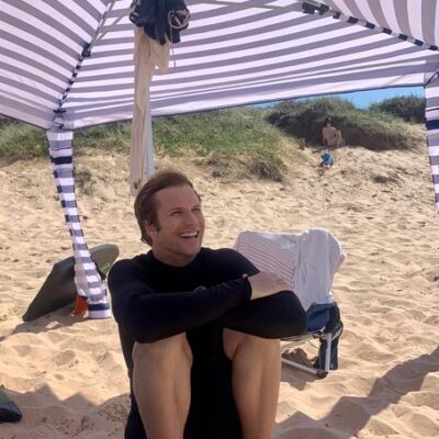 A young man sitting under an umbrella at the beach