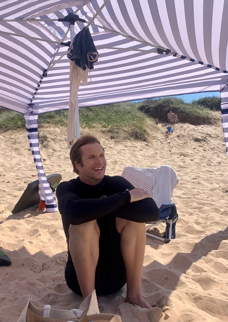 A young man sitting under an umbrella at the beach