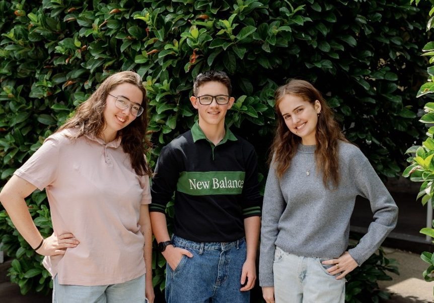 A group of young people stand in front of a tree smiling