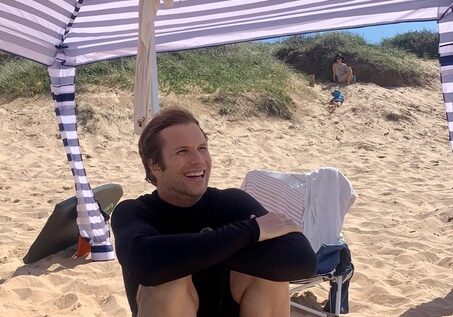 A young man sitting under an umbrella at the beach
