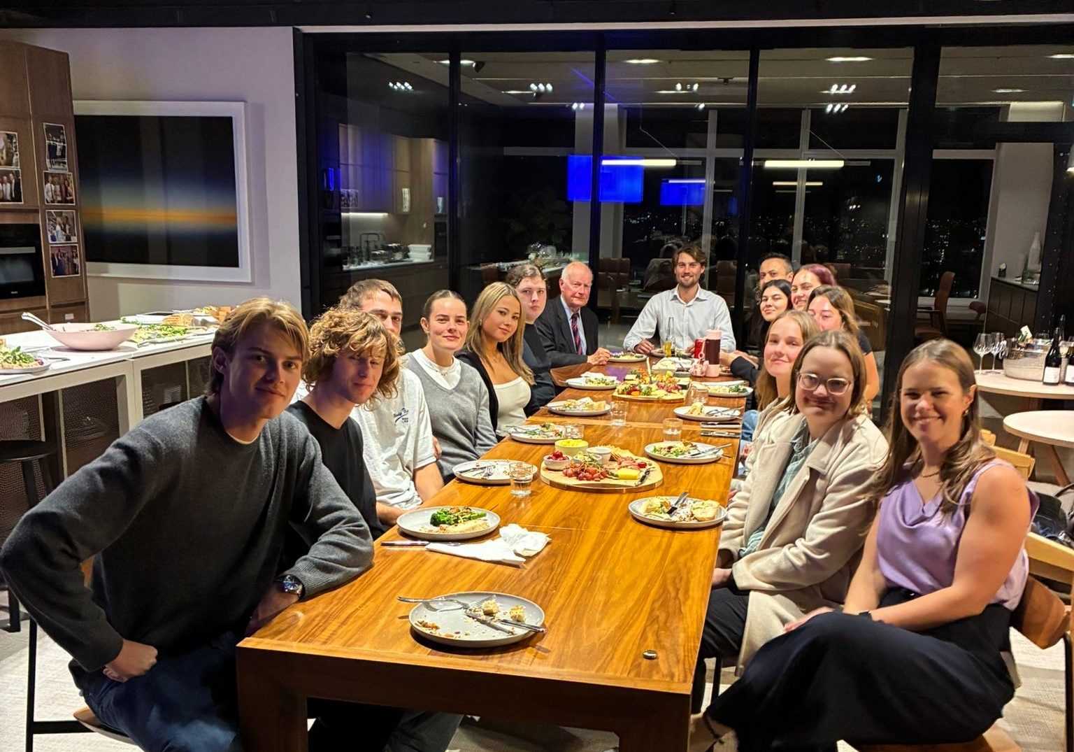 A large group sit at a long table enjoying a meal