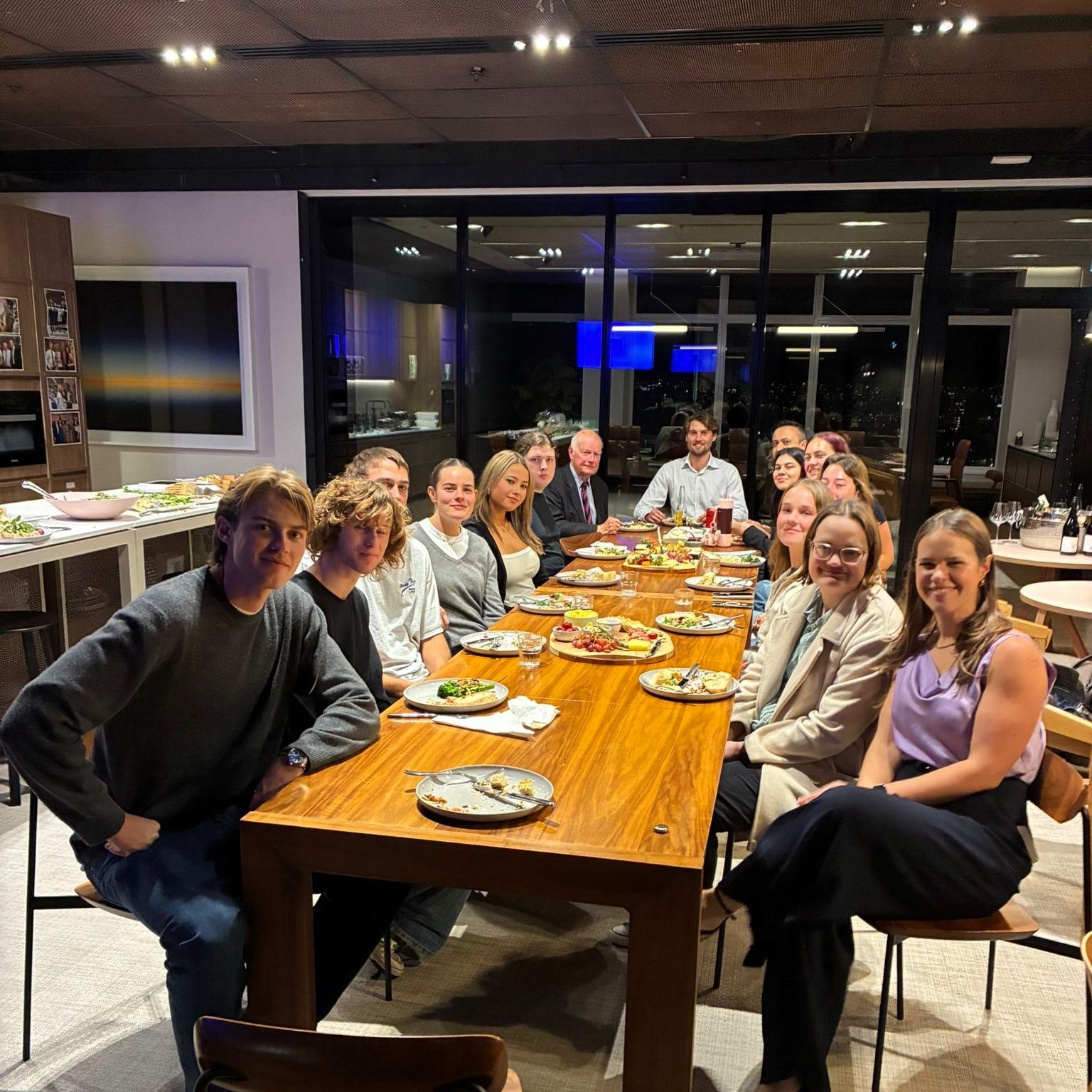 A large group sit at a long table enjoying a meal