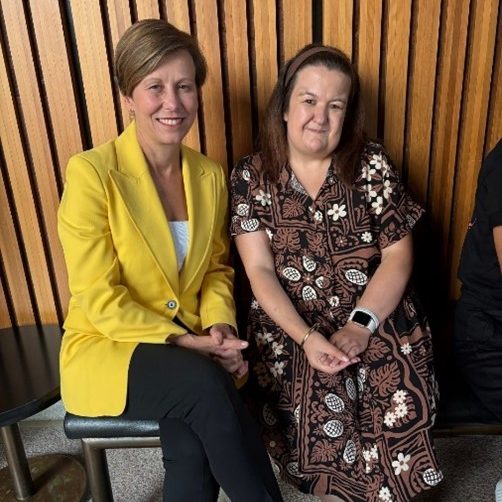 Two women sitting together in front of a paneled wall