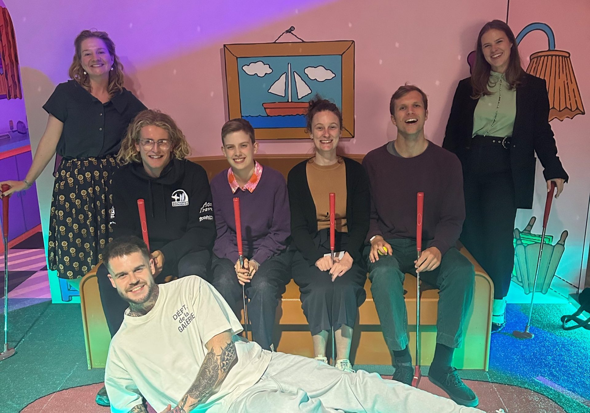 A group of people sitting on a lounge holding mini golf sticks
